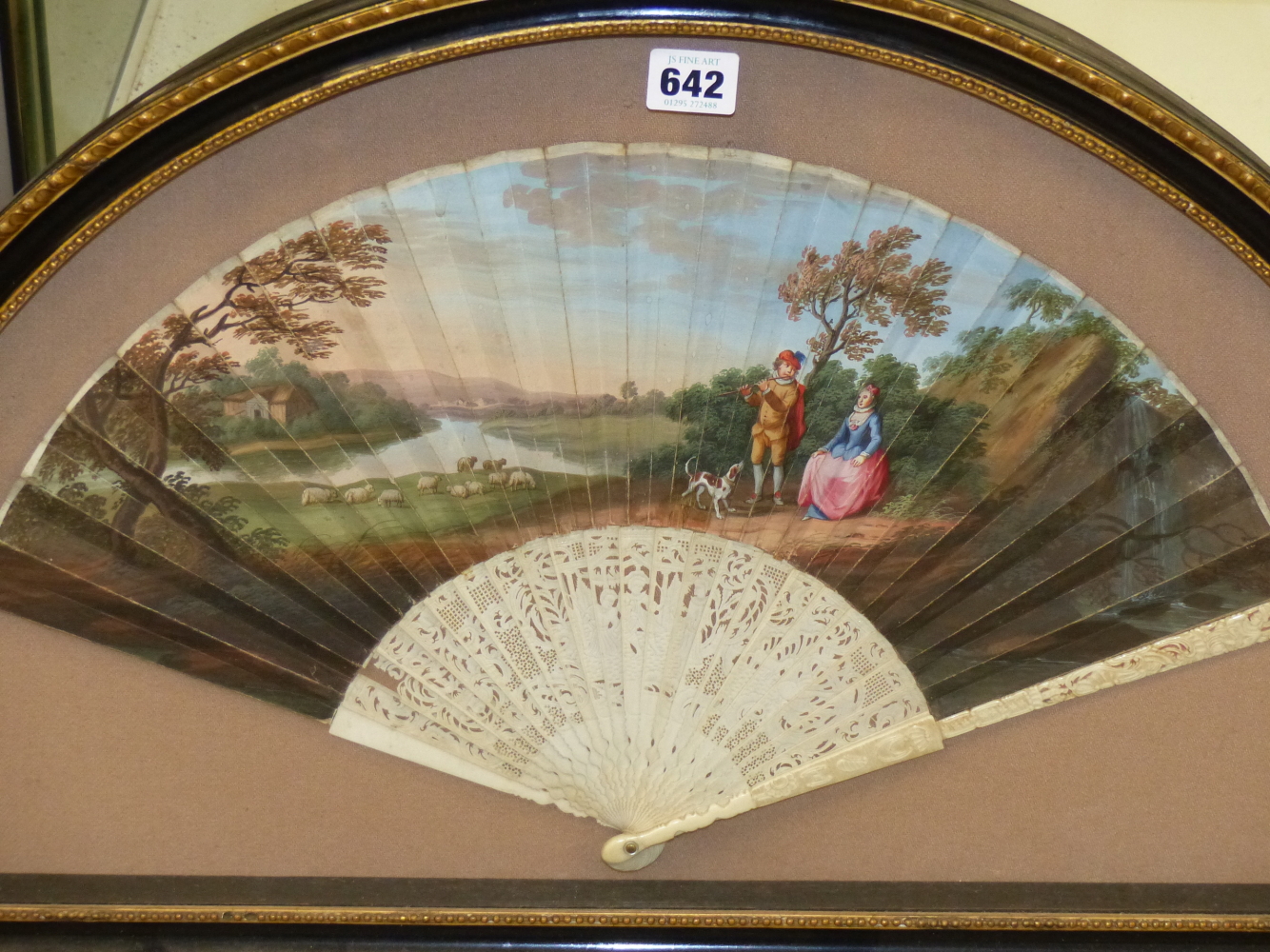 A FRAMED FAN WITH THE LEAF PAINTED WITH A FLAUTIST ENTERTAINING A LADY SEATED BEFORE SHEEP GRAZING