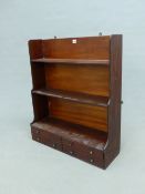 A WALL HANGING MAHOGANY WATERFALL BOOK CASE WITH TWO BANKS OF TWO DRAWERS BELOW THE BOTTOM OF THE