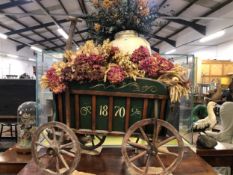 A GREEN PAINTED FOUR WHEEL HAND DRAWN CART FILLED WITH DRIED FLOWERS AND SEEDS ABOUT A DOULTON STONE