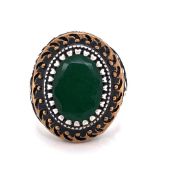 A GENTS OVAL CUT GREEN GEMSTONE SIGNET RING IN A CARVED SILVER BLACK AND GILDED HEAVY MOUNT.