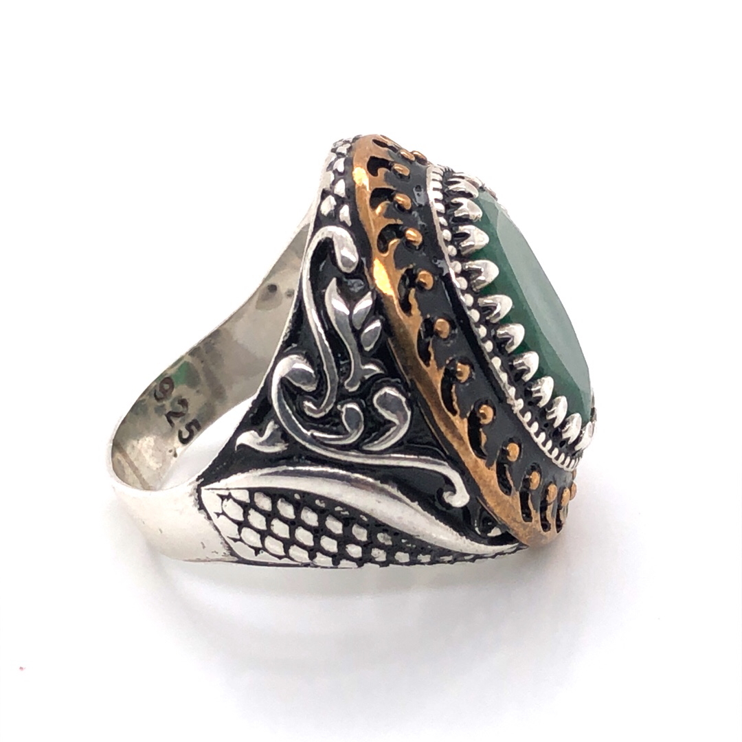 A GENTS OVAL CUT GREEN GEMSTONE SIGNET RING IN A CARVED SILVER BLACK AND GILDED HEAVY MOUNT. - Image 2 of 2