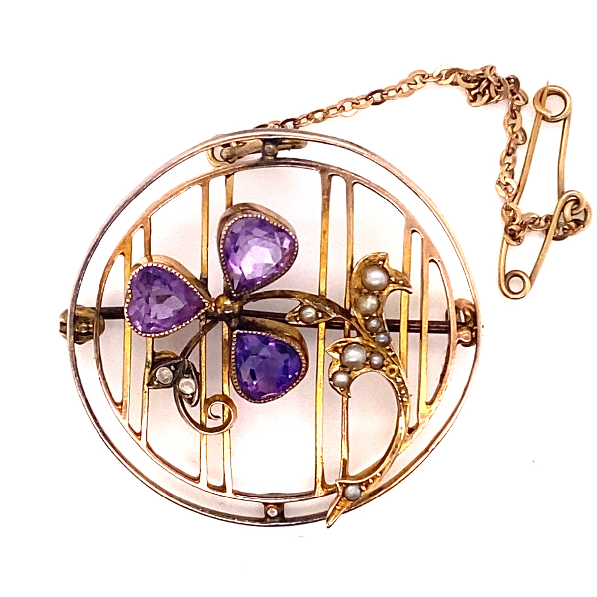 AN EDWARDIAN AMETHYST AND SEED PEARL OPENWORK BROOCH WITH ATTACHED SAFETY CHAIN. THE THREE PEAR