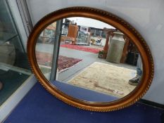 AN OVAL GILT FRAME WALL MIRROR.