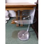 A ROUND GLASS TOPPED TABLE ON CHROME BRACKET AND FOOT