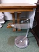 A ROUND GLASS TOPPED TABLE ON CHROME BRACKET AND FOOT