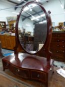 AN OVAL DRESSING TABLE MIRROR ON MAHOGANY THREE DRAWER SERPENTINE BASE