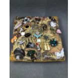 AN ASSORTED COLLECTION OF BROOCHES DISPLAYED ON A VINTAGE WOVEN CUSHION. TOTAL NUMBER OF BROOCHES