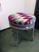 A GREEN PAINTED METAL FOUR LEGGED STOOL ON CASTER FEET, THE ROUND SEAT UPHOLSTERED