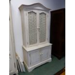 A CREAM PAINTED CABINET WITH GRILLE DOORS RECESSED ABOVE PANELLED DOORS. W 100 x D 50 x H 214cms.