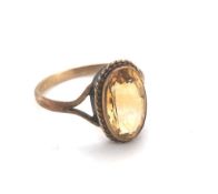 AN OVAL FACETED CITRINE SOLITAIRE RING IN A RUB OVER SETTING WITH A ROPE EDGE BORDER. UNHALLMARKED