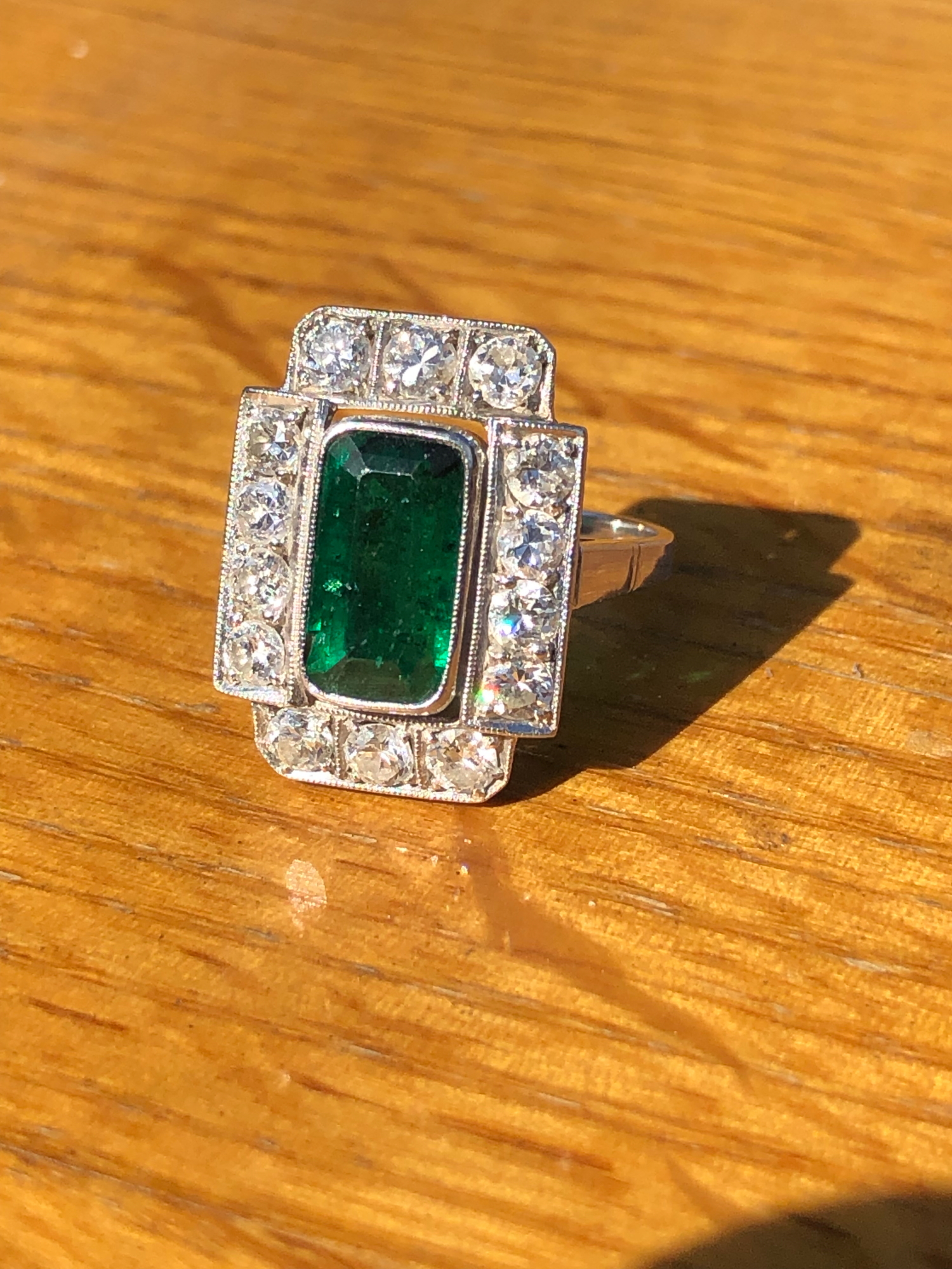 AN ART DECO EMERALD AND DIAMOND PANEL RING. THE LOZENGE SHAPE EMERALD APPROX 11 X 6mm, SURROUNDED BY