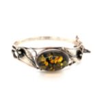 AN AMBER AND SILVER HALLMAKRED ART NOUVEAU STYLE HINGED BANGLE. THE OVAL AMBER IN A FOLIATE