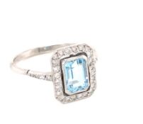 AN AQUAMARINE AND DIAMOND HALO SET DRESS RING. THE CENTRAL AQUAMARINE IN A BEZEL SETTING