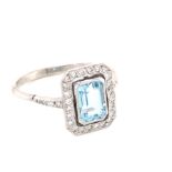 AN AQUAMARINE AND DIAMOND HALO SET DRESS RING. THE CENTRAL AQUAMARINE IN A BEZEL SETTING