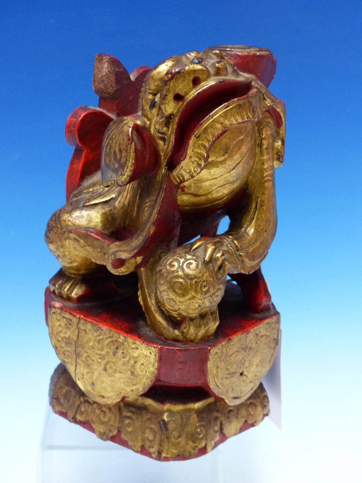 A CHINESE CARVED WOOD LION SEATED WITH A BROCADE BALL PARCEL GILT ON A RED LACQUER GROUND. H 23cms.
