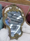 A SHAPED MIRROR IN GILT ROCOCO FRAME CRESTED BY A CABOCHON CENTRED TREFOIL. 68 x 46cms.