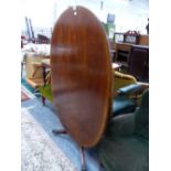 A CROSS BANDED MAHOGANY OVAL TILT TOPPED TABLE ON A BALUSTER COLUMNAND TRIPOD WITH BRASS PAW