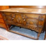 AN OAK SIDE BOARD, THE TWO DOORS CARVED WITH A ROUND ARCH MOTIFS, THE TURNED LEGS JOINED BY A