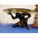 A SMOKEY GLASS OVAL TOPPED TABLE SUPPORTED BY A NUBIAN FIGURE ON ON KNEE. W99 x D 63 x H 52cms.