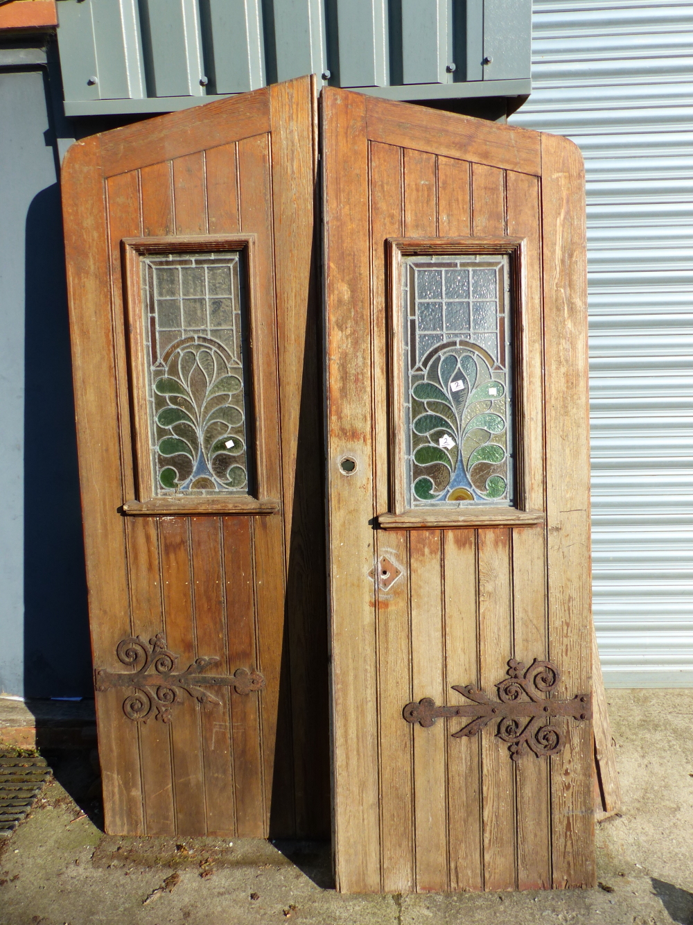 A PAIR OF GOTHIC OAK DOORS WITH FAUX STRAP HINGES AND STAINED GLASS PANELS COMPLETE WITH SURROUND.