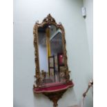 AN OGEE ARCHED GIRANDOLE WITH TWO CANDLESTICKS ABOVE A RED VELVET SHELF, THE GILT FRAME WITH FOLIAGE