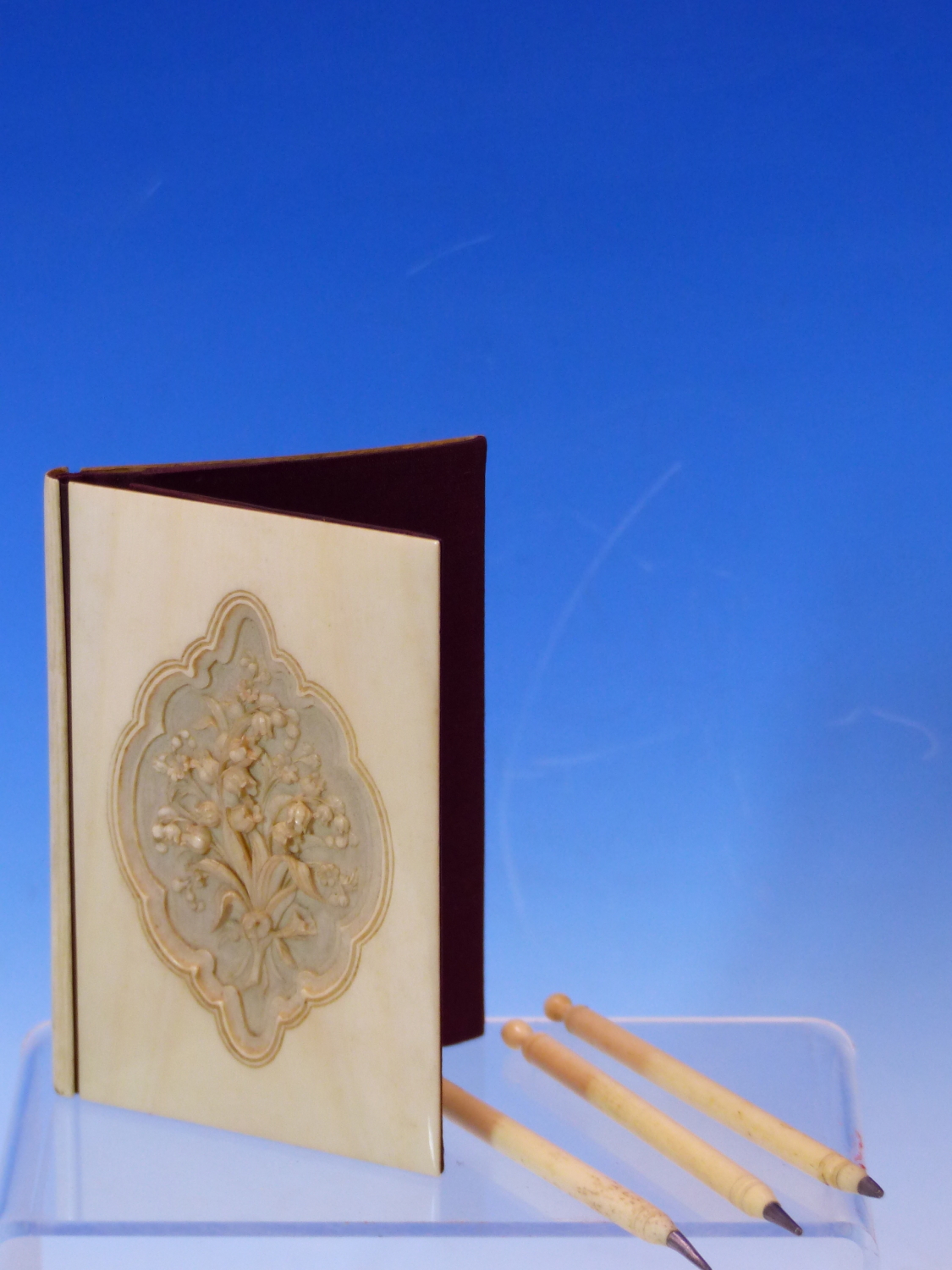 AN ANTIQUE IVORY NOTE CASE CARVED WITH A VIGNETTE OF A BUNCH OF FLOWERS TOGETHER WITH FOUR STYLUSES
