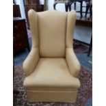 A WING ARMCHAIR UPHOLSTERED IN BEIGE, THE MAHOGANY SQUARE SECTION LEGS TAPERING TO CASTER FEET.