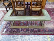 A BRASS CLUB FENDER WITH THE GREEN LEATHER SEAT SUPPORTED ON TUBULAR COLUMNS AND PLINTH FOOT. W