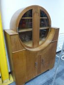 AN ART DECO OAK CABINET, THE TWO DOORS TO THE CIRCULAR TOP GLAZED OVER SHELVES, A FLUTED BAND