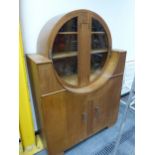 AN ART DECO OAK CABINET, THE TWO DOORS TO THE CIRCULAR TOP GLAZED OVER SHELVES, A FLUTED BAND