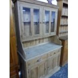 A 20th C. PINE DRESSER, THE TWIN PANELLED DOORS TO THE TOP GLAZED OVER SHELVES, THE BASE WITH
