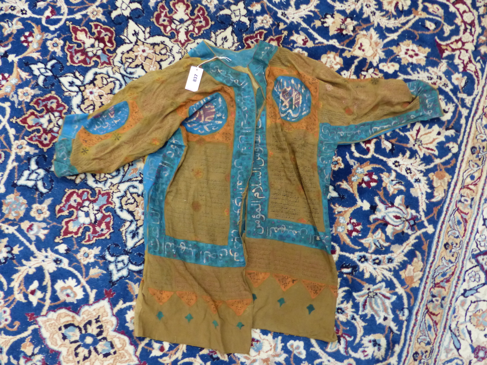 AN ISLAMIC TALISMANIC BROWN TUNIC PAINTED WITH BLUE EDGING AND ORANGE DETAILS ABOUT INSCRIPTIONS