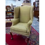 A 19th C. WING ARMCHAIR UPHOLSTERED IN OLIVE GREEN, THE CABRIOLE FRONT LEGS CARVED WITH LEAVES AT