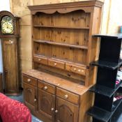 A SMALL PINE DRESSER WITH THREE DOORS AND DRAWERS AND THRE FURTHER TO THE RACK.