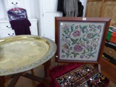 AN EASTERN BRASS DISH TOPPED FOLDING TABLE, A RED BORDERED VELVET FLORAL PANEL AND AN OAK FRAMED