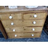 A VICTORIAN PINE CHEST OF TWO SHORT AND THREE LONG DRAWERS EACH WITH WHITE CERAMIC KNOB HANDLES ABOV