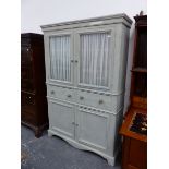 A GREY PAINTED WOODEN CABINET, THE GLAZED DOORS ENCLOSING SHELVES ABOVE TWO DRAWERS AND DOORS