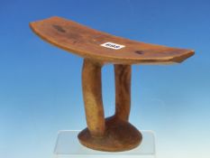 AN EAST AFRICAN CARVED WOODEN HEADREST, THE PUNT SHAPE RAISED ON TWO ARMS ABOVE THE DOMED CIRCULAR