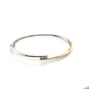 A 9ct HALLMARKED YELLOW AND WHITE GOLD HINGED BANGLE WITH THREE CHANNEL SET BRILLIANT CUT