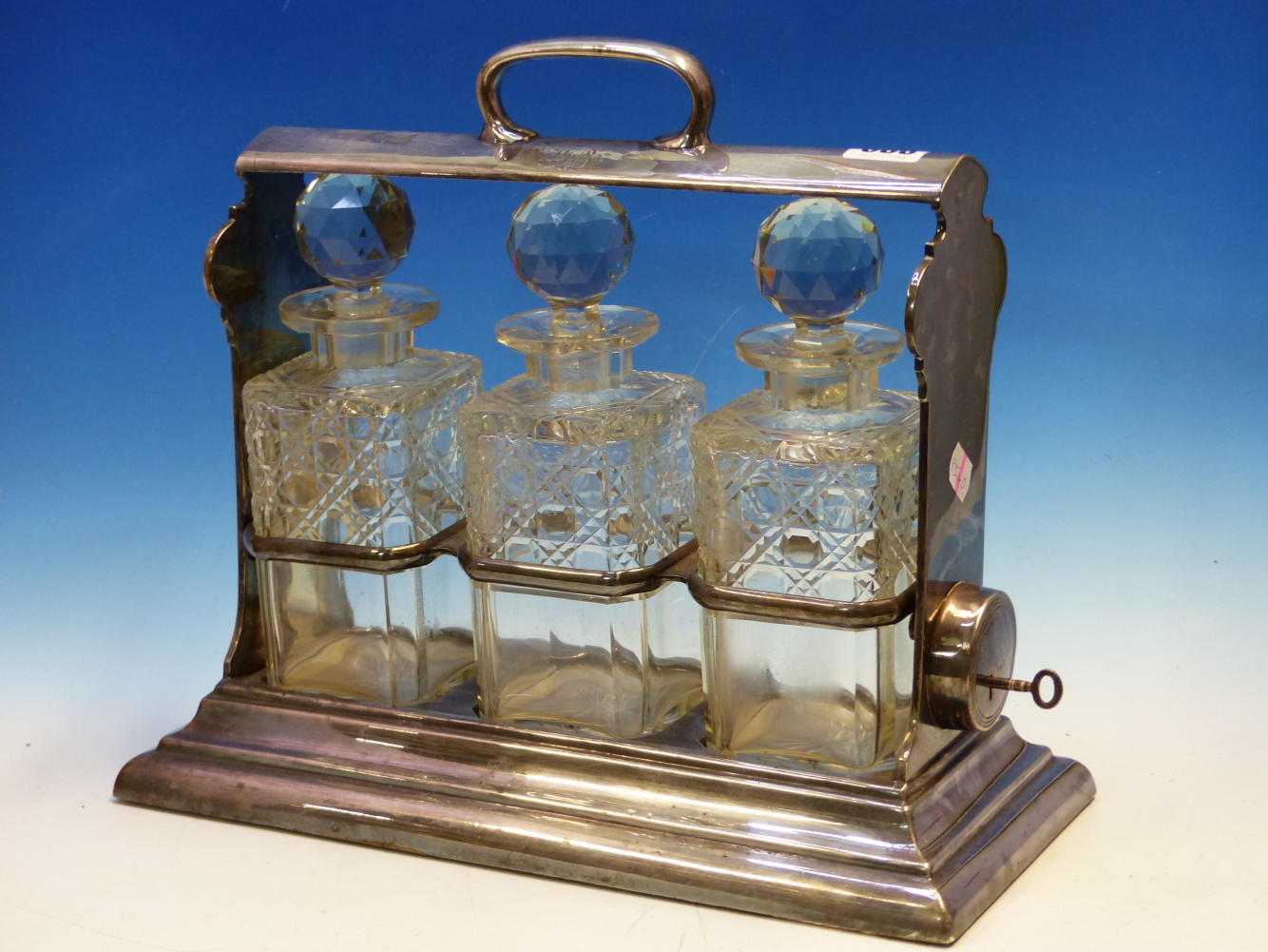 A VINTAGE ELECTROPLATE THREE BOTTLE TANTALUS, THE LOCK TO ONE SIDE BELOW THE CARRYING HANDLE ALLOWIN