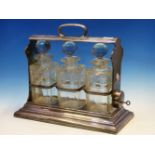 A VINTAGE ELECTROPLATE THREE BOTTLE TANTALUS, THE LOCK TO ONE SIDE BELOW THE CARRYING HANDLE ALLOWIN