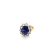 AN 18ct GOLD HALLMARKED SAPPHIRE AND DIAMOND CLUSTER RING. THE OVAL FACETED BLUE SAPPHIRE APPROX 6.