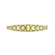 A VICTORIAN STYLE HINGE BANGLE, SET WITH NINE GRADUATED OVAL GREEN PERIDOT. BUTTON CLASP WITH SAFETY