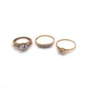 THREE CUBIC ZIRCONIA DRESS RINGS. TWO SINGLE SOLITAIRES AND A FIVE STONE HALF ETERNITY RING. SIZES