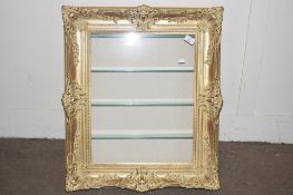 GLAZED WALL DISPLAY CABINET FORMED AS AN ORNATE GILT PICTURE FRAME WITH GLASS SHELVES WITHIN,