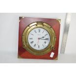 MARINE CLOCK FORMED AS A PORTHOLE MOUNTED ON A MAHOGANY BACK PLATE, APPROX 30CM SQUARE