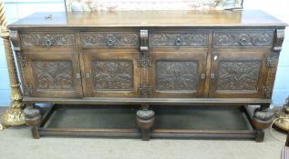 Large 20th century oak sideboard in baronial style, having a plain top over four carved fronted
