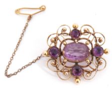 Antique amethyst set brooch in an Etruscan style of open work scroll design, centring an oval cut