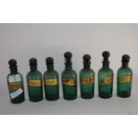 Group of small green glass chemists drug jars with stoppers and titles in gilt lettering (7),