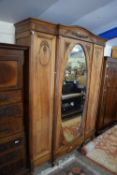 EARLY 20TH CENTURY BREAK FRONT TRIPLE WARDROBE WITH EMPIRE STYLE CARVED DECORATION, RAISED ON TURNED